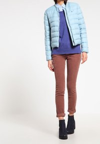 Jasnoniebieska kurtka puchowa, niebieski sweter, brązowe spodnie z kordurowej tkaniny i czarne botki za kostkę. Kurtka ma zamek z przodu i ściągacze przy rękawach.