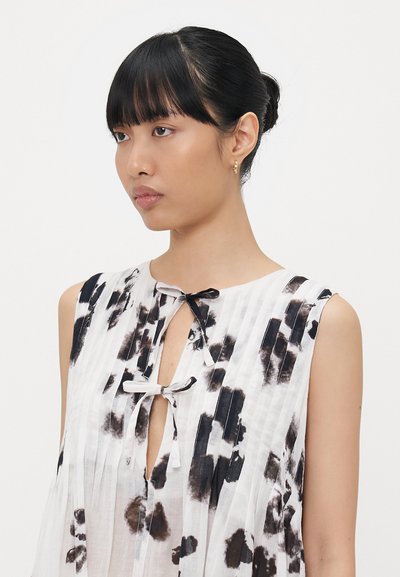 Abito bianco con motivi tie-dye neri, design senza maniche e pieghe verticali. Apertura a chiave nota sul collo con dettaglio a fiocco.