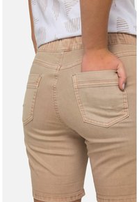 Shorts in denim beige con un texture liscia, caratterizzati da due tasche posteriori e una vita cucita. Orlo tagliato all'altezza della coscia.