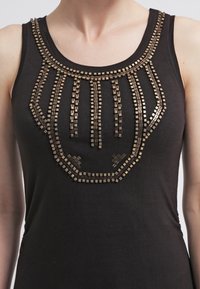 Zwarte tanktop met een decoratieve halslijn, versierd met metalen vierkante studs die in een geometrisch patroon zijn gerangschikt. Gladde stofstructuur.