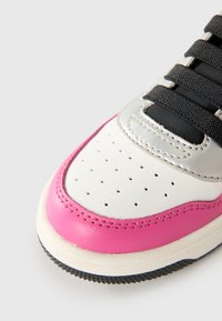Baskets basses avec une base en cuir blanc, des accents roses et un panneau argenté métallique. Dotées de lacets noirs et de détails perforés sur le bout.