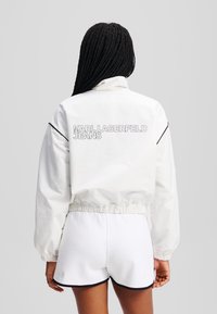 Witte windjack met elastische manchetten en tailleband, met een logo op de achterkant dat "KARL LAGERFELD JEANS" leest.