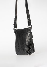 Svart läder crossbody-väska med mjuk textur, justerbara remmar och spännelement. Har en dragkedjestängning för säker förvaring.