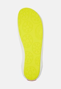 Suola di una scarpa realizzata in un materiale gommato giallo brillante con motivi rotondi e un bordo laterale bianco. Superficie testurizzata per una migliore aderenza.