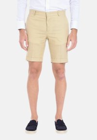 Pantaloni corti in lino beige chiaro con taglio dritto, risvolti e tasche frontali, abbinati a espadrillas blu scuro.