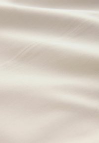 Tissu lisse de couleur crème avec des plis subtils et une texture douce, mettant en valeur son tissage fin et son ton neutre.