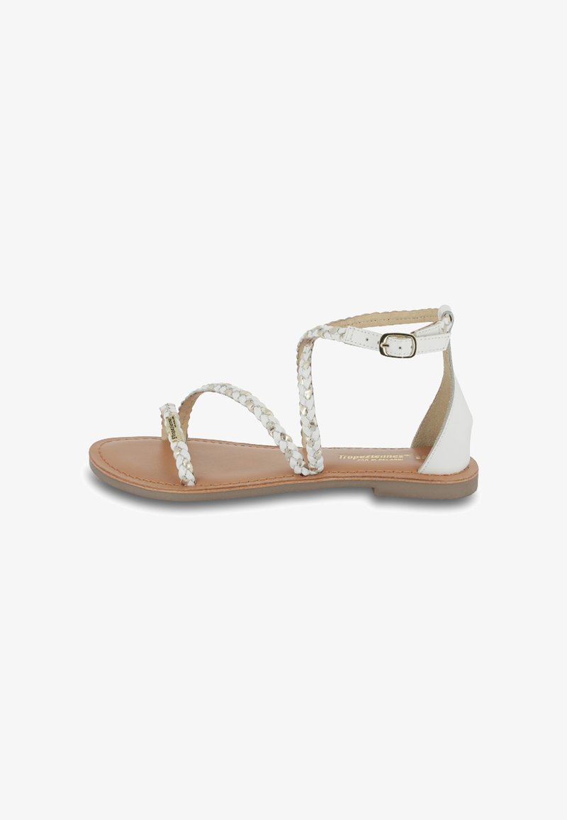 Sandales blanches tressées avec une semelle plate, dotées d'une fermeture à boucle et d'une semelle intérieure lisse de couleur marron clair. Design simple et accents minimaux.