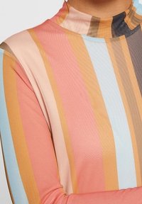 Bluzka z długim rękawem i wysokim kołnierzem, wykonana z lekkiego, rozciągliwego materiału. Posiada pionowe paski w odcieniach różu, niebieskiego, pomarańczowego i brązowego.
