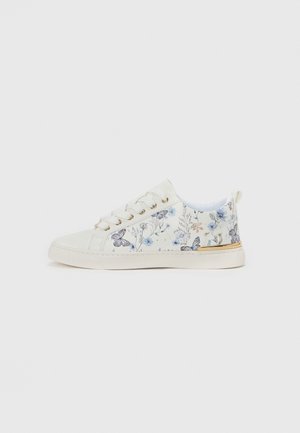 Hvid lavtop sneaker med blomstret og sommerfugleprint, guld-øjer og gyldent accent på hælen, på en ensfarvet lys baggrund.