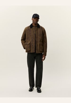 Brown patterned jacket with a black collar, featuring two front pockets. Paired with black pants and shiny shoes. Worn with a black cap.