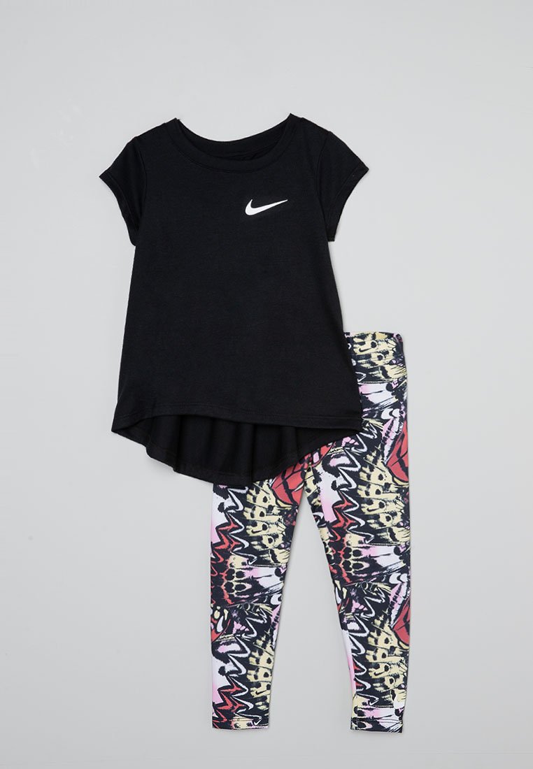 T-shirt noir à manches courtes avec un logo Nike blanc, associé à des leggings colorés et à motifs présentant des designs abstraits dans des tons de rose et de jaune.
