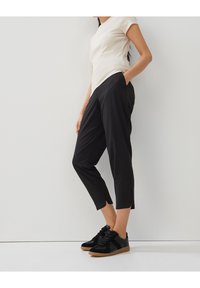 Pantalons noirs coupés avec poches latérales, fabriqués en tissu lisse. Associés à un haut beige ajusté à manches courtes côtelées et à des baskets noires.