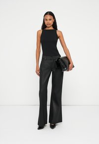 Top senza maniche nero a costine abbinato a pantaloni neri a vita alta e gamba larga; tiene una clutch nera testurizzata; tessuto morbido, silhouette elegante.
