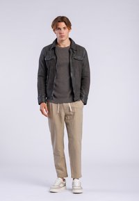 Chaqueta de cuero negra con acabado texturizado, suéter de punto gris con canalé, pantalones de lino beige y zapatillas de color claro. Ajuste casual, con un detalle mínimo.