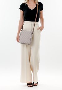 Borsa quadrata di colore grigio chiaro con motivo a diamante, tracolla in pelle marrone e rifiniture nere. Il modello indossa un top nero e pantaloni larghi color beige.