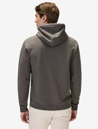 Grå bomullshoodie med ett rymligt huva. Har ribbade muddar och fåll, släta sömmar och en mjuk textur. Bakifrån syns en minimal design.