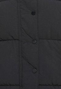 Tela acolchada negra con costuras verticales y tres botones de presión negros redondos en una fila vertical.
