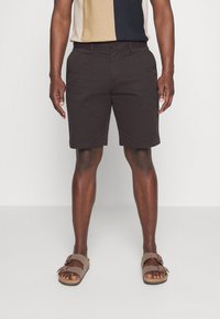 Donkerbruine shorts van lichtgewicht stof, met een rechte snit en riemlussen, gecombineerd met bruine sandalen voor een casual look.