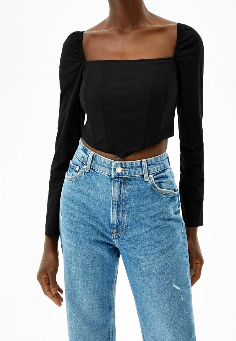 Svart kortärmad topp med fyrkantig halsringning och rynkade axlar, kombinerad med högmidjade ljusblå jeans med slitna detaljer.