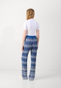 White short-sleeve top paired with blue and white zigzag-patterned wide-leg pants. The pants feature a smooth waistband and flowing fabric.