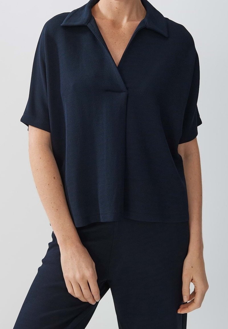 Haut à manches courtes marine avec un col, tissu texturé, coupe décontractée et un subtil détail croisé à l'avant.