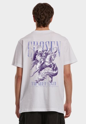 Vue de dos d'une personne portant un t-shirt blanc avec un dessin violet représentant un guerrier ailé à cheval terrassant un dragon et le texte "CHOISI POUR DÉFENDRE."