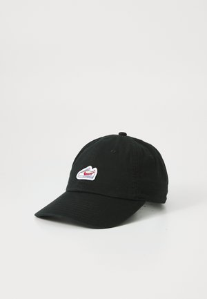 Cappello in cotone nero con visiera curva, con un piccolo logo ricamato di una sneaker in bianco e rosso sulla parte anteriore. Cinturino regolabile sul retro.