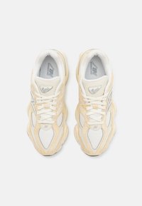 Sneaker bianche e crema realizzate in mesh e suede. Presentano un design a onda distintivo, lacci e un logo argentato riflettente.