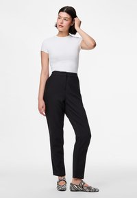 Top branco de manga curta combinado com calças pretas ajustadas e sapatos de slip-on com padrão de zebra, exibindo uma silhueta ajustada e linhas limpas.