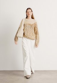 Beige, fluffy genser med oversize passform, vide hvite bukser og en lys beige håndveske. Myk tekstur, vide ermer og minimalistisk design.