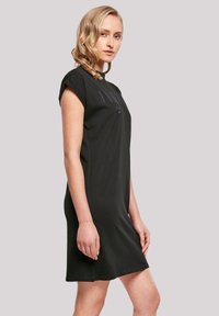 Schwarzes, kurzärmliges Kleid mit lockerer Passform. Glatte Textur mit minimalem Branding auf der Brust und geradem Saum.