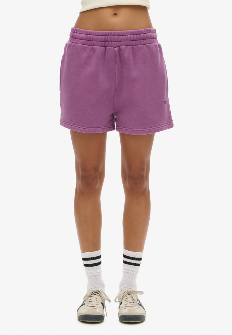 Lila Baumwollmischung-Shorts mit einem elastischen Bund, seitlichen Taschen und gesticktem Saum. Getragen mit weiß-schwarz gestreiften Socken und Turnschuhen.