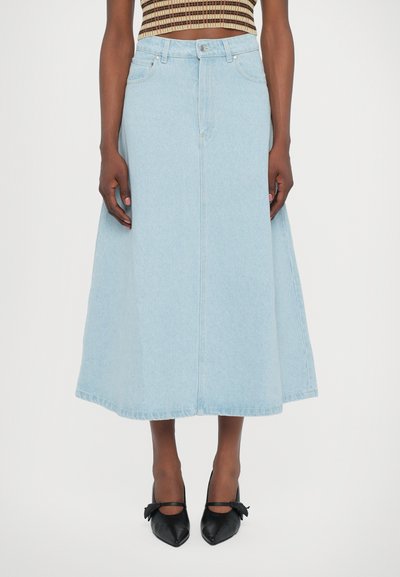 Lyseblå denim maxi-nederdel med en løs silhuet, knaplukning og to frontlommer. Båret med sorte spidse sko.