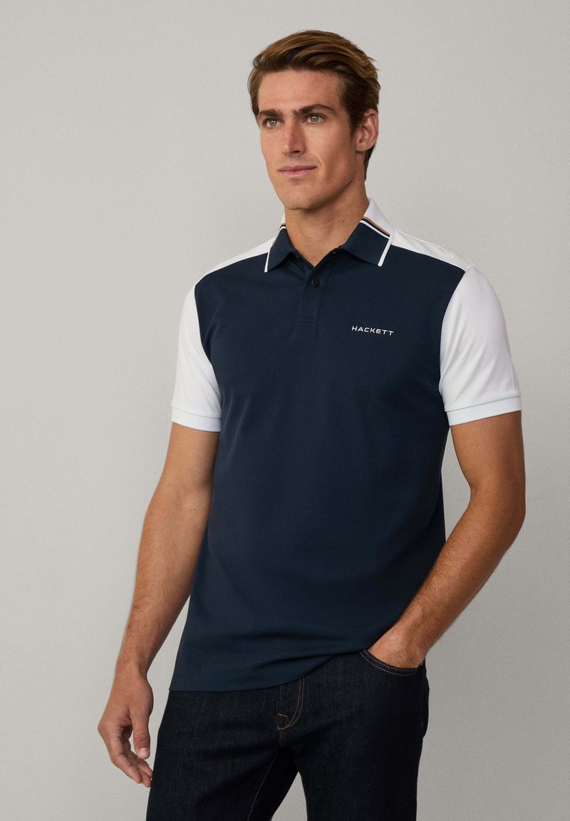 Polo de color azul marino con mangas cortas blancas, cuenta con un cuello con rayas horizontales y un logotipo impreso en el pecho.