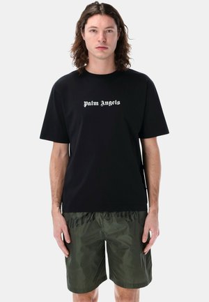 T-shirt di cotone nero con il testo "palm Angels" in bianco sul petto, abbinato a pantaloni verde con una texture lucida e stampa del logo.