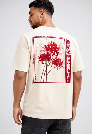 Mann trägt ein cremefarbenes Hemd mit rotem Spinnenlilien-Blumenmotiv und den Texten „Red Spider Lilies“, „Afterlife“ und japanischen Schriftzeichen auf dem Rücken.