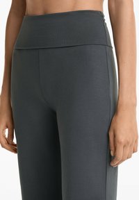 Nahaufnahme der Taille eines Models, das hochgeschnittene, dunkelgraue Leggings trägt, mit glattem Stoff und elastischem Bund.