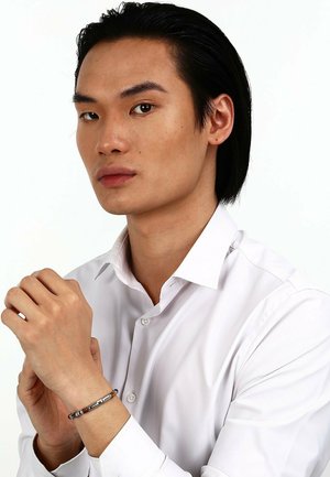 Silver bracelet with metallic accents worn on a hand. Model in a white button-up shirt. Smooth texture, neutral color palette.