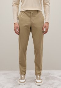 Chinos caqui hechos de tela ligera, con corte slim, frente plano y trabillas para cinturón. Llevados con zapatillas blancas y beige.