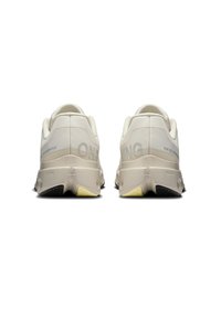 Baskets de sport beiges avec des surfaces texturées, une marque bien visible et un accent jaune sur la semelle ; col rembourré pour le confort.