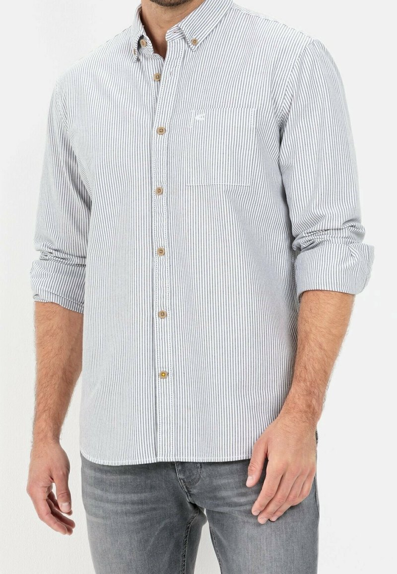 Chemise à rayures bleues et blanches avec poche poitrine et manches retroussées ; boutons en bois et texture de tissu douce.