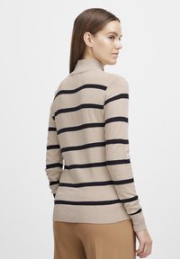 Maglione a maglia beige con righe orizzontali nere, colletto alto, maniche lunghe e polsini e orlo a costine. Texture liscia.