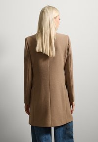 Bruine wollen mixjas met een getailleerd design, lange mouwen en een rechte snit. Beschikt over een centrale achternaad en een soepele textuur.