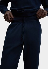 Joggers a righe blu navy con una texture morbida, dotati di vita elasticizzata e cordino. Vista ravvicinata che evidenzia la posizione delle mani.