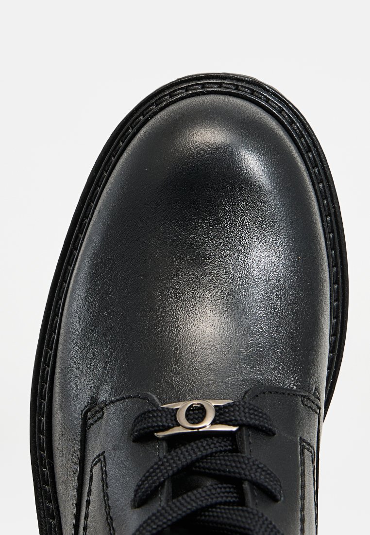 Schwarzer Leder-Schuh mit abgerundetem Zeh, der eine glatte Textur, schwarze Schnürsenkel und eine kleine metallische Akzentierung über den Schnürsenkeln aufweist.