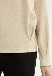 Beżowy, długi rękaw, top o teksturowanym dzianinie, z bocznymi rozcięciami, luźnym kroju i ściągaczami przy mankietach, w połączeniu z czarnymi, dopasowanymi spodniami.