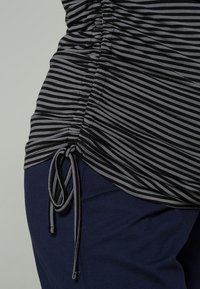 Top listrado em preto e cinza com textura franzida e detalhe de cordão na barra, combinado com calças azul-escuro. Tecido suave, design casual.