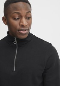 Black cotton sweater with a high collar, featuring a half zipper and a silver pull tab. Smooth texture without visible patterns or accents.