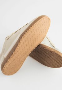 Beige-tennari kum puu-vaidusega, mustriga tallaga ja tekstureeritud külgedega. Nauhat ja õmblused täiendavad disaini.