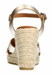 Wedge sandal with a metallic gold back strap, tan footbed, and woven jute heel. The heel features a textured, natural rope design.